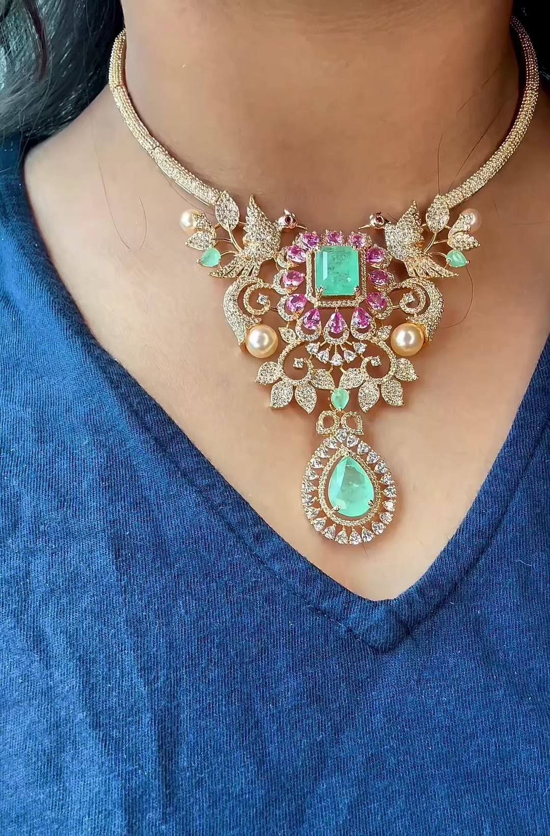 Close-up of gold plated necklace with pastel pink and mint green stones, crystals and teardrop pendant